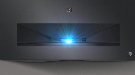 Projektør 4K HDR mat sort rektangulær med blåt lys fra midten af skærmen, på mørk grå baggrund
