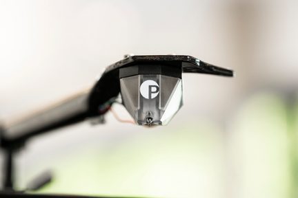 Detailní záběr na průhledné a černé plastové zařízení s bílým kruhovým logem obsahujícím písmeno "P", připevněné k kovové konstrukci