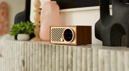 Stolní reproduktor z ořechu, zlatá kovová čelní strana s diagonální mřížkou, kruhový displej, otočný knoflík, pohled ze tří čtvrtin