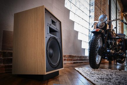 Højttaler i lys træ, sort front med stor woofer og horn, set i trekvarts underopstilling