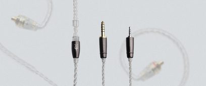 Tre 3,5 mm jackstik med guldbelægning i forskellige længder, hængende på lysegrå flettede kabler