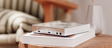 Tragbarer silberner CD-Player in Dreiviertelansicht, auf einem weißen Buch auf einem Holztisch platziert