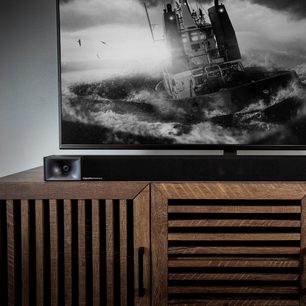 Klipsch Cinema 400 træ-soundbar under en skærm, der viser et sort-hvidt billede af en båd på et oprørt hav