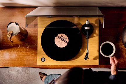 Svetlý drevený gramofón s priehľadným krytom, čiernou vinylovou platňou a ramenom vpravo, prepínač 33/45, pohľad zhora