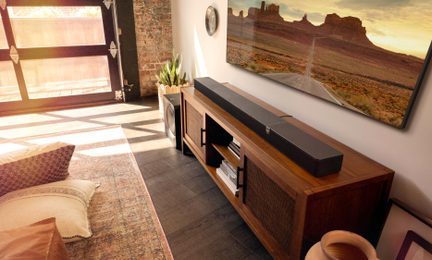 Černý soundbar se subwooferem vedle dřevěného TV stolku v moderním, světlém obývacím pokoji