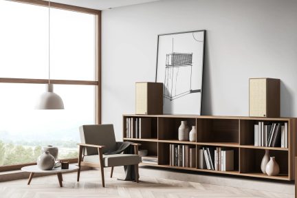 Madal puidust avatud sektsioonidega raamaturiiul raamatute, kõlarite ja dekoratsiooniga minimalistlikus elutoas