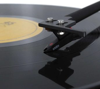 Ortofon pladespiller på sort drejearm med to sølvfarvede knapper, på en sort og grå vinylplade