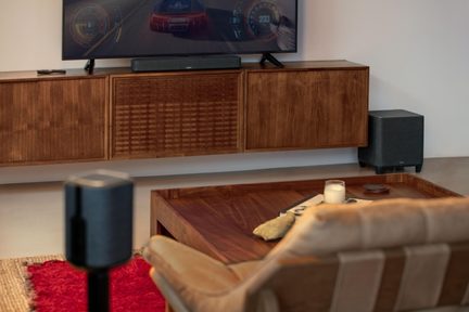 Black soundbar with subwoofer and rear speaker, wood-design living room, TV on wall-mounted unit