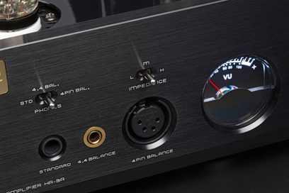 Primo piano, vista frontale, sulla facciata in alluminio spazzolato nero del preamplificatore per cuffie hi-fi Cayin HA-3A argento, con prese jack dorate da 6,35 mm e 4,4 mm, connettore XLR a 4 poli, due interruttori a levetta metallici e un VU-metro rotondo retroilluminato