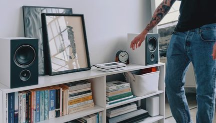 Niska biała półka w salonie z książkami, głośnikami hi-fi i dekoracją, mężczyzna w dżinsach stojący obok