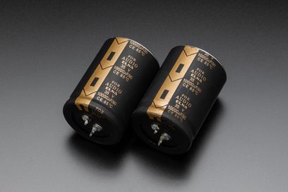 Two gold-colored Marantz AV 10 electrolytic capacitors for home theater preamp, shown in front view against a dark gray background