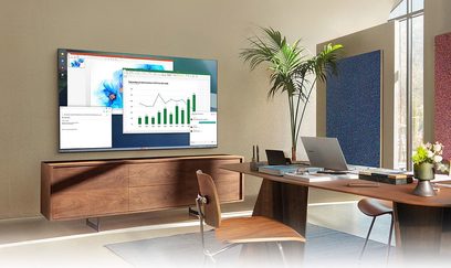 Skrivebord med Samsung QE43Q65A 2021-skærm, der viser grafer, TV-møbel i træ, grøn indendørsplante