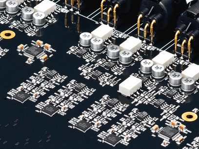 Zwarte printplaat met zilveren en gouden elektronische componenten, witte cilindrische condensatoren, bovenaanzicht van dichtbij
