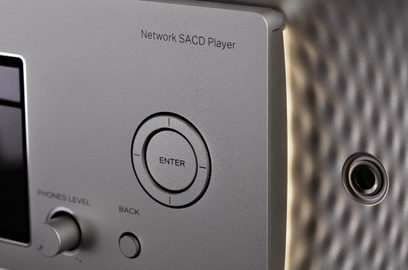 Nærbilde av frontpanelet på en SACD-nettverksspiller, Enter-knapp, hodetelefonutgang og høyttalergrill, med metallisk grå overflate