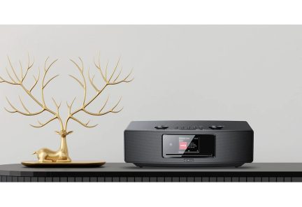 Gyldent objekt i form af en hjort med store gevirer, sort radio med skærm og knapper, set forfra, på en sort overflade