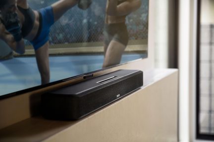 Compact black Denon TV soundbar placed under a flat-screen TV in a bright living room