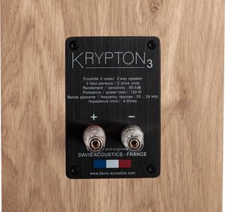 Knihovní reproduktor Krypton 3 Nordik (bílý), černý obdélníkový zadní panel s bílým textem, 2 průhledné svorky, světlé dřevěné pozadí
