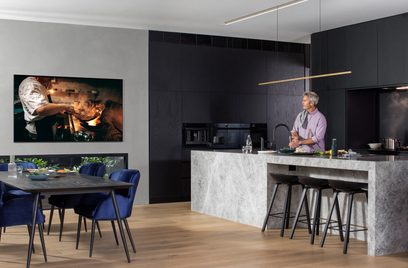 Moderne keuken met centraal marmeren eiland, zwarte kasten, man die een maaltijd bereidt en Samsung-tv met vlambeeld