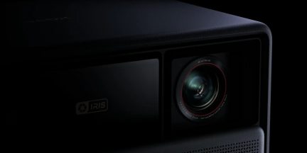 Črn projektor 4K Ultra HD, prikazan pod tričetrtinskim kotom, z objektivom z rdečim obročem in logotipom IRIS