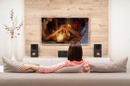 Moderní obývací pokoj s nástěnnou televizí a domácím kinem, žena zezadu sedící na béžové pohovce