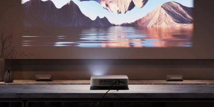 Videoproiettore a ottica ultra corta grigio su mobile TV, proiezione di un paesaggio di montagna e lago su grande schermo