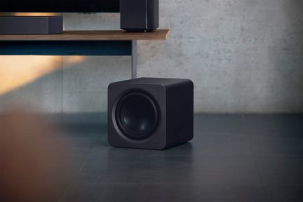 Mattschwarzer Subwoofer mit glattem Gehäuse, abgerundeten Ecken und sichtbarem, zentral platziertem Rundlautsprecher, Ansicht aus drei Vierteln von vorne