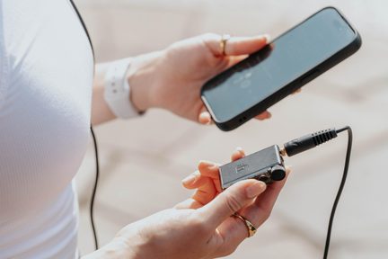 Primo piano di mani con smartphone nero e lettore audio portatile nero in metallo con texture, cavo jack da 3,5 mm collegato