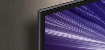 Primo piano a tre quarti sull’angolo superiore destro di uno schermo piatto, cornice in metallo grigio antracite spazzolato con bordo interno nero e pannello che mostra un motivo viola striato