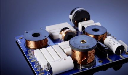 Filtre passif pour enceinte audio, carte bleue avec bobines cuivrées et condensateurs blancs, vue de trois quarts