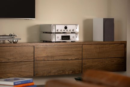 Zilverkleurige Marantz hi-fi versterkers frontaal gezien op houten meubel, zwarte luidspreker rechts