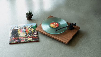 Un tourne-disque en bois avec un vinyle transparent, une pochette d'album colorée et une petite plante dans un pot brun