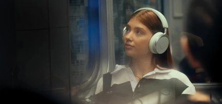 Vita over-ear-hörlurar burna av en kvinna som sitter i tunnelbanan, sedd i profil