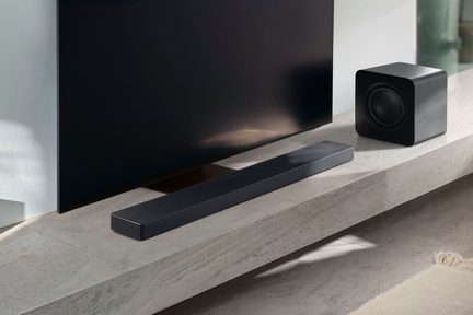 Černý soundbar s perforovaným kovovým vrchním dílem doplněný černým matným subwooferem s kulatými hranami, pohled ze tří čtvrtin shora