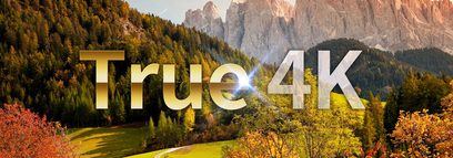 Tekst "True 4K" på et landskab med bjerge, nåleskov og eng om efteråret med farverigt løvfald