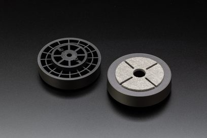 Top-down view of two cylindrical metal pieces, one with a radial grille and the other with an engraved cross