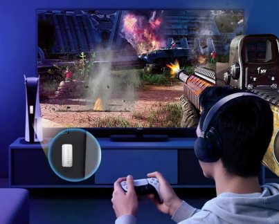 Adaptor audio Questyle negru, cu un jucător cu căști și un controler în fața unui ecran de joc și a unei console PS5