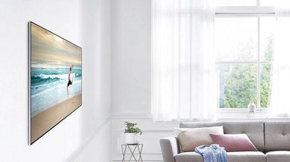 Samsung-fladskærm monteret på væggen i en lys stue, der viser et billede af bølger, der bryder på en sandstrand