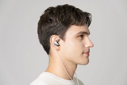 Højre profil af et mandligt ansigt med sølvfarvede in-ear-hovedtelefoner og en hvid ledning, lys grå baggrund