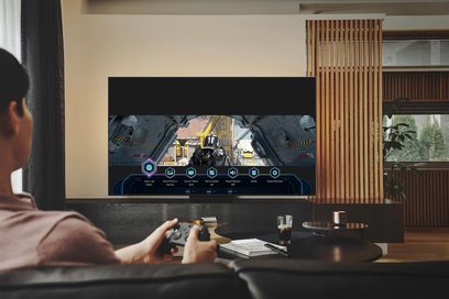 Samsung QE50QN90B 2022 fladskærms-TV, der viser et first-person shooter-videospil, styret af en gamekontrol holdt i hænder