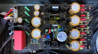 Indvendigt syn af en elektronisk enhed med printplader, gyldne kondensatorer og røde og sorte stik