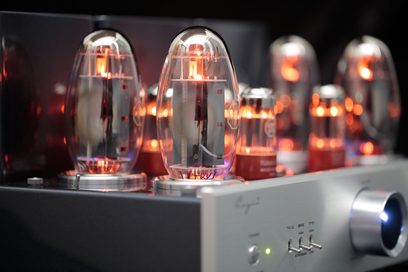 Integrovaný stereo lampový zesilovač Cayin CS-150A v černé barvě, detailní pohled ze tří čtvrtin zepředu ukazující žhavící skleněné lampy, přední panel z kartáčovaného stříbrného hliníku, ovládací knoflík hlasitosti obklopený modrým světlem a černý kovový rám.