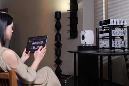 Hi-fi-system i silver på svart rack med vit högtalare, styrning från surfplatta i ett vardagsrum