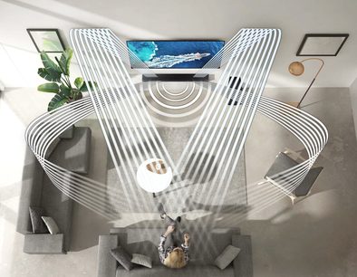 Moderne stue med grå sofa, hvidt sofabord, gulvlampe, grønne planter og et fladskærms-tv, der viser et billede af havet og klipper