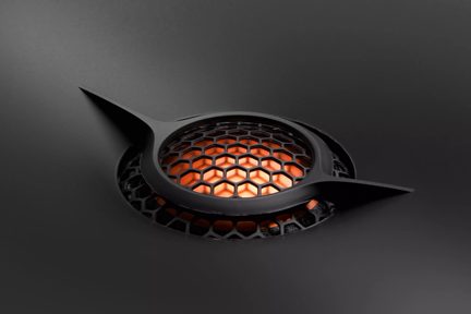 Zwarte luidspreker met honingraatdesign, fel oranje kegel onder ronde grille, close-up bovenaanzicht