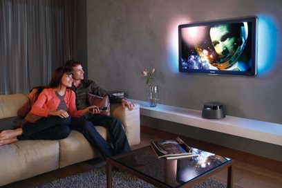 Philips CTS4000-fjernsyn, der viser et rumligt billede, placeret på et møbel foran en sofa, hvor en mand og en kvinde sidder