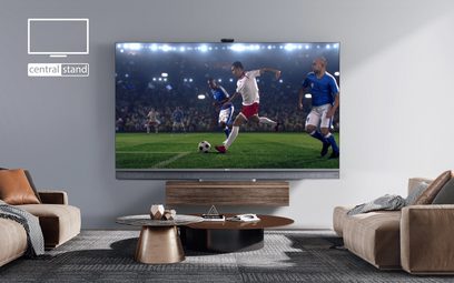 TCL 65C821-fjernsyn, der viser en fodboldkamp i en moderne stue med sofaer og et træbordmøbel
