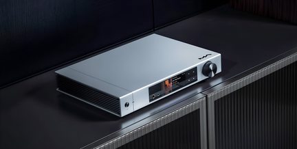 Audioförstärkare i borstad aluminium med silverfinish, trekvarts vy uppifrån, frontpanel med central färgskärm, hörlursuttag och touchknappar, stor svart volymratt till höger, vänster sida med ventilationsribbor