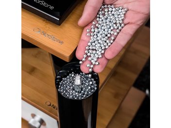 Palline metalliche argentate disposte in cerchio su una mano che regge un involucro nero in legno, con il logo "Norstone" inciso