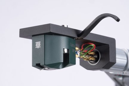 Dark green resin phonostage mounted under a matte black metal cartridge holder with a curved finger lift, gold connectors, and visible colored wiring, close three-quarter view