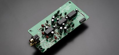 Grønt printplade med sorte og røde elektroniske komponenter, tæt ovenfra-udsigt på ensfarvet grå baggrund